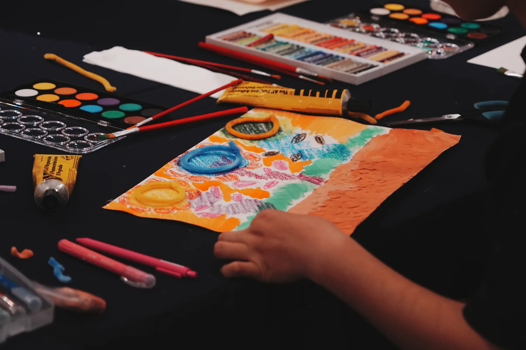 Paint, pastel and modelling materials surrounding an expressive artwork in progress